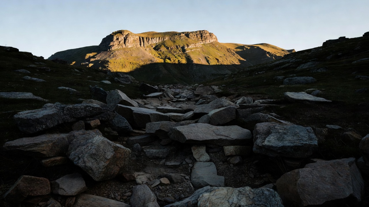 Shadowed foreground stones leading toward a distant sunlit mountain ridge